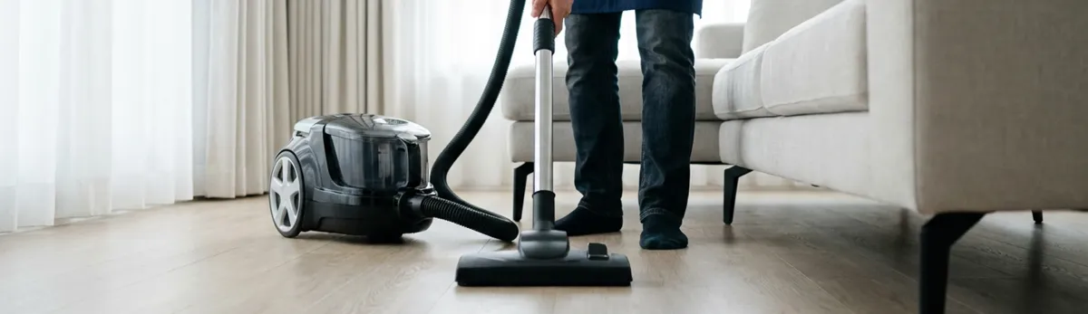 Professional house cleaner vacuuming a living room floor with a canister vacuum cleaner, Huntsville, AL.