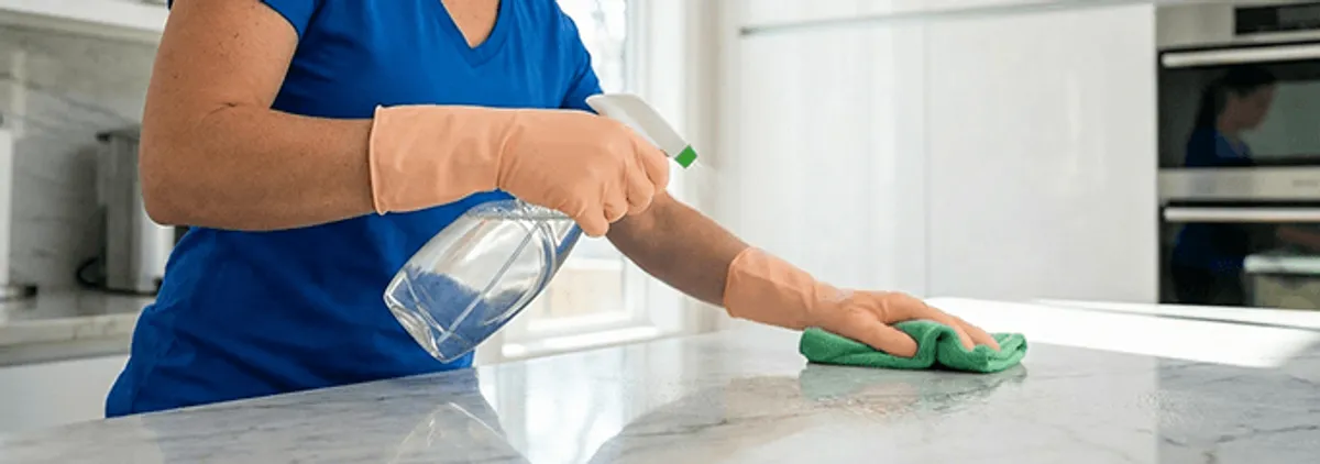 Maid service worker spraying and wiping a kitchen countertop with a microfiber cloth for sanitizing, Huntsville, AL.